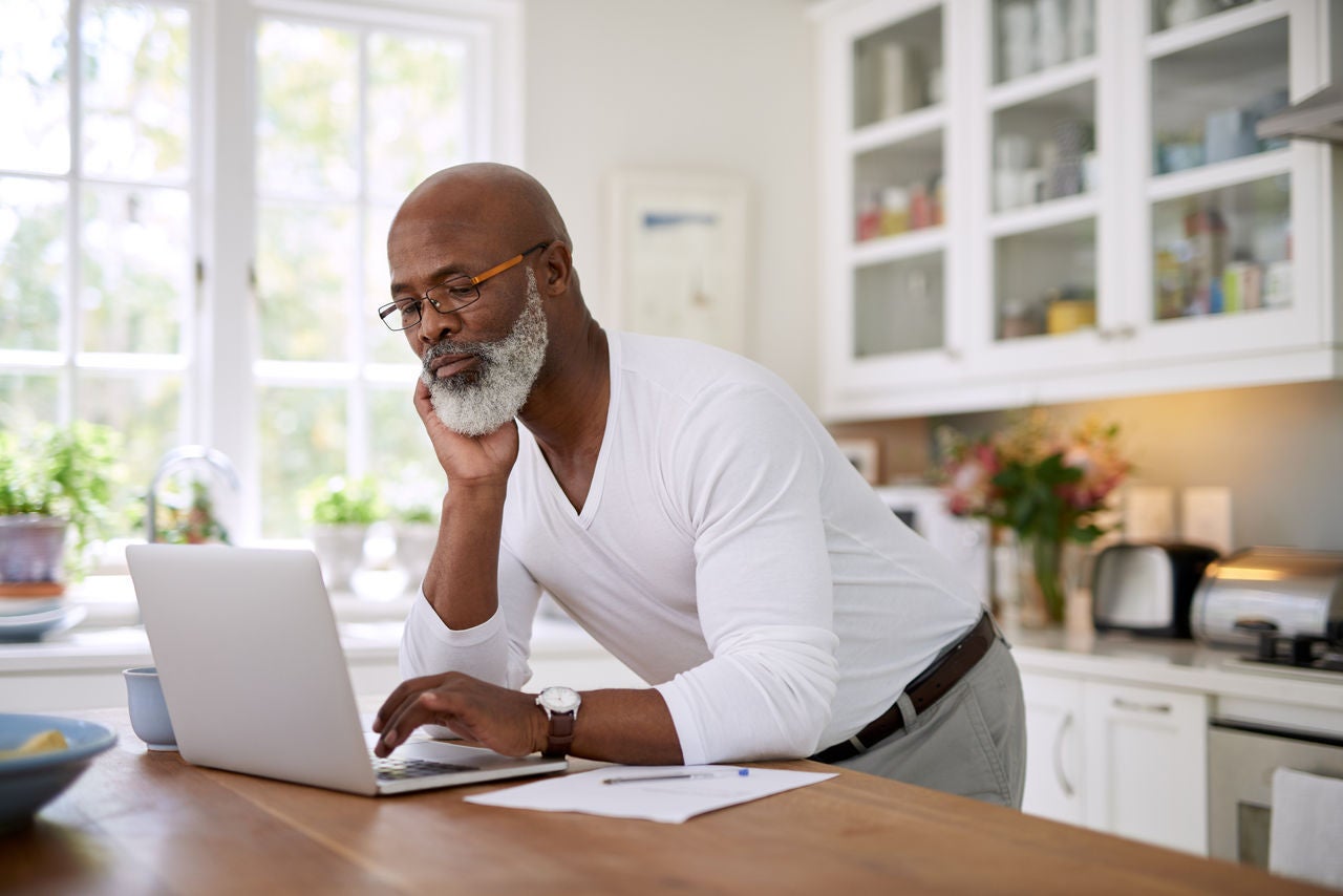 Shot of a mature man using a laptop while working out his finances at home